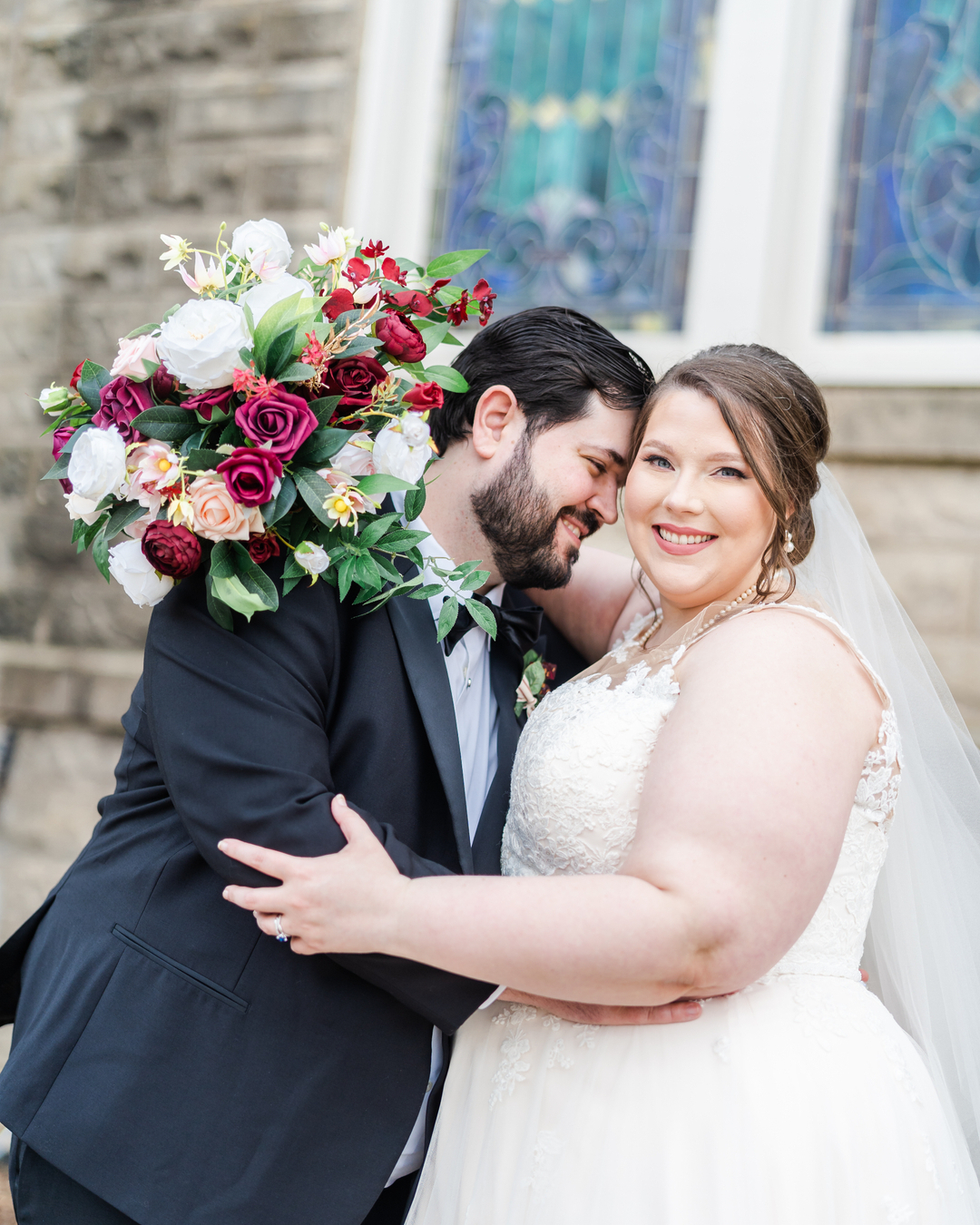 bride and groom embracing in front church stained glass windows